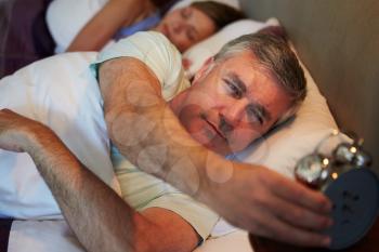 Couple In Bed With Man Reaching To Switch Off Alarm Clock