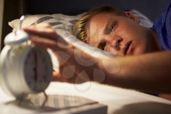 Teenage Boy Waking Up In Bed And Turning Off Alarm Clock
