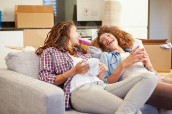 Two Women Relaxing On Sofa With Hot Drink In New Home