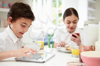 Schoolchildren With Digital Tablet And Mobile At Breakfast