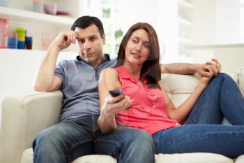 Bored Husband Sitting With Wife On Sofa Watching TV