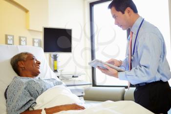 Doctor With Digital Tablet Talks To Woman In Hospital Bed