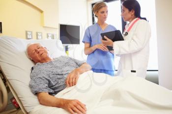 Medical Team Meeting As Senior Man Sleeps In Hospital Room