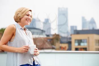 Young Woman Relaxing On Roof Terrace With Cup Of Coffee
