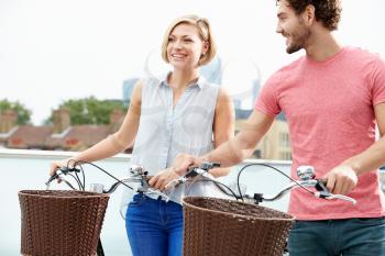 Couple Pushing Bikes With City Skyline In Background