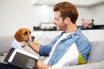 Man Looking At Paperwork And Playing With Pet Dog At Home