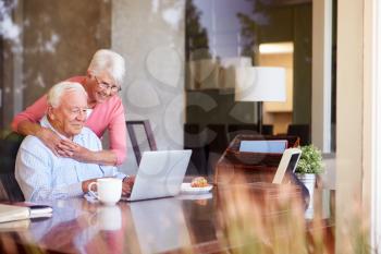 Senior Couple Using Laptop On Desk At Home