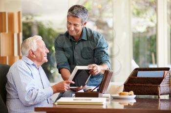 Senior Father Looking At Photo In Frame With Adult Son