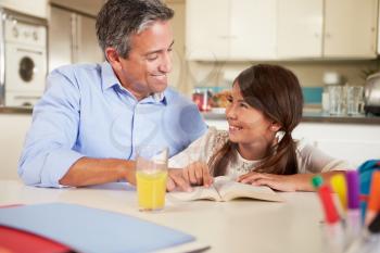 Father Helping Daughter With Reading Homework At Table