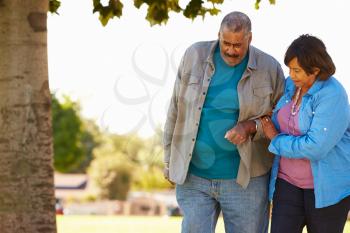 Senior Woman Helping Husband As They Walk In Park Together