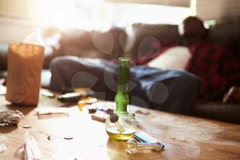 Man Slumped On Sofa With Drug Paraphernalia In Foreground