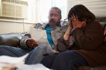 Worried Senior Couple Sitting On Sofa Looking At Bills