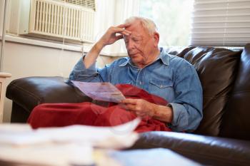 Worried Senior Man Sitting On Sofa Looking At Bills