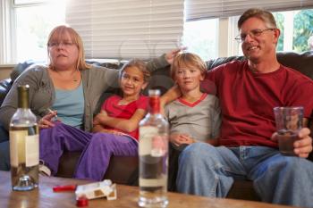 Parents Sit On Sofa With Children Smoking And Drinking