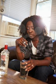 Woman Sitting On Sofa With Bottle Of Vodka And Cigarettes