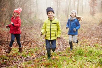 Three Children Running Through Winter Woodland