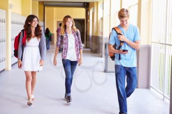 High School Students Walking In Hallway Using Mobile Phone