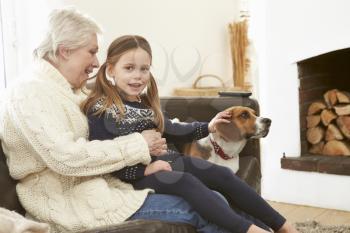 Grandmother And Granddaughter Relaxing At Home With Pet Dog