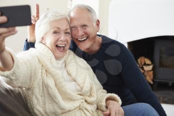 Senior Couple Sitting On Sofa Taking Selfie