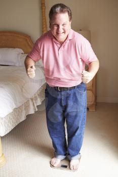 Happy Overweight Man Standing On Scales In Bedroom