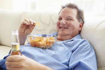Overweight Man At Home Eating Chips And Drinking Beer