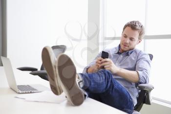Man Using Mobile Phone At Desk In Design Studio