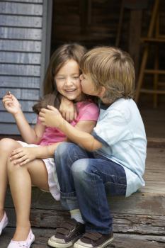 Young boy kissing sister on veranda