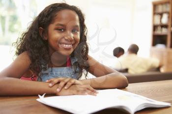 Girl Reading Book For Homework At Table