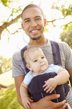 Father With Son In Baby Carrier Walking Through Park
