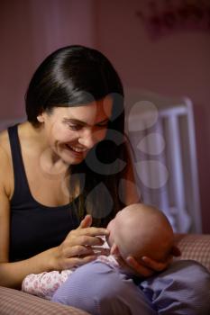 Mother At Home Cuddling Newborn Baby In Nursery