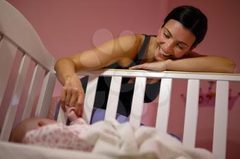 Mother Playing Game With Newborn Baby In Cot