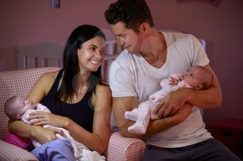 Parents At Home Cuddling Twin Baby Daughters In Nursery