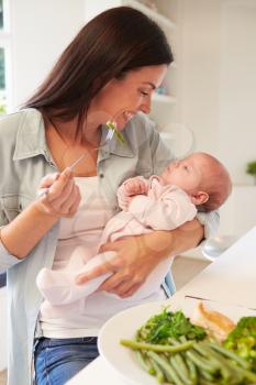Mother With Baby Eating Healthy Meal In Kitchen