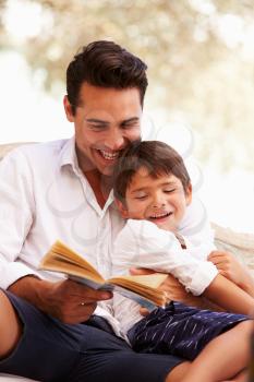 Father And Son Sitting In Garden Reading Book Together