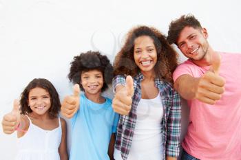 Family Standing Outdoors Against White Wall Giving Thumbs Up