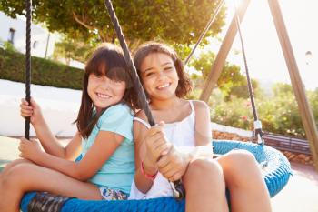 Two Girls Having Fun On Swing In Playground