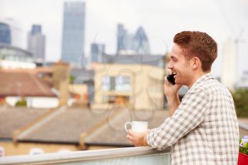 Man Using Mobile Phone On Rooftop Garden Drinking Coffee