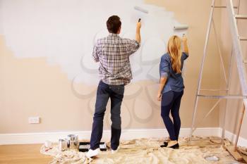 Couple Decorating Room Using Paint Rollers On Wall