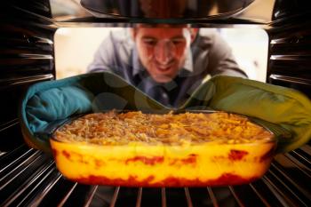 Man Putting Dish Of Lasagne Into Oven To Cook