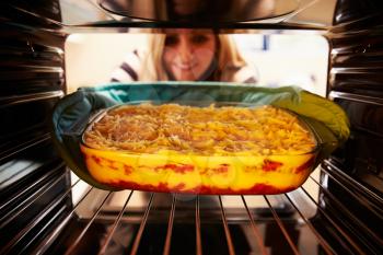 Woman Putting Dish Of Lasagne Into Oven To Cook