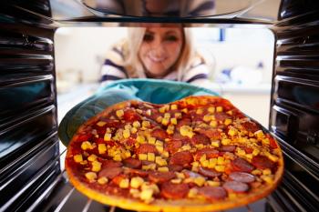 Woman Putting Pepperoni Pizza Into Oven To Cook