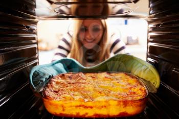 Woman Taking Cooked Dish Of Lasagne Out Of The Oven