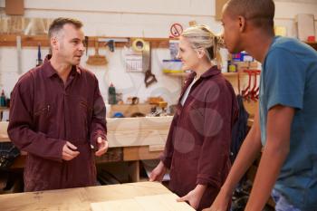 Carpenter Talking To Apprentices In Carpentry Workshop
