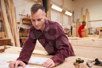 Carpenter Looking At Plans In Workshop