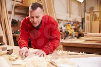 Carpenter Planing Wood In Workshop