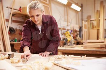 Female Apprentice Planing Wood In Carpentry Workshop