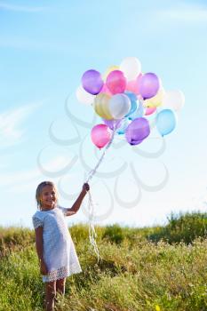 Young Girl Holding Bunch Of Colorful Balloons Outdoors