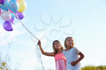 Two Young Girls Holding Bunch Of Colorful Balloons Outdoors
