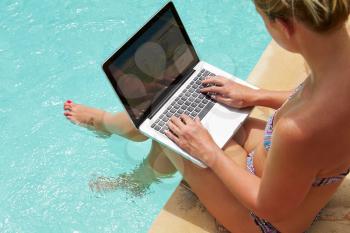 Woman Using Laptop Whilst Dangling Feet In Swimming Pool