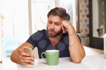 Young Man Drinking Coffee And Using Mobile Phone At Home
